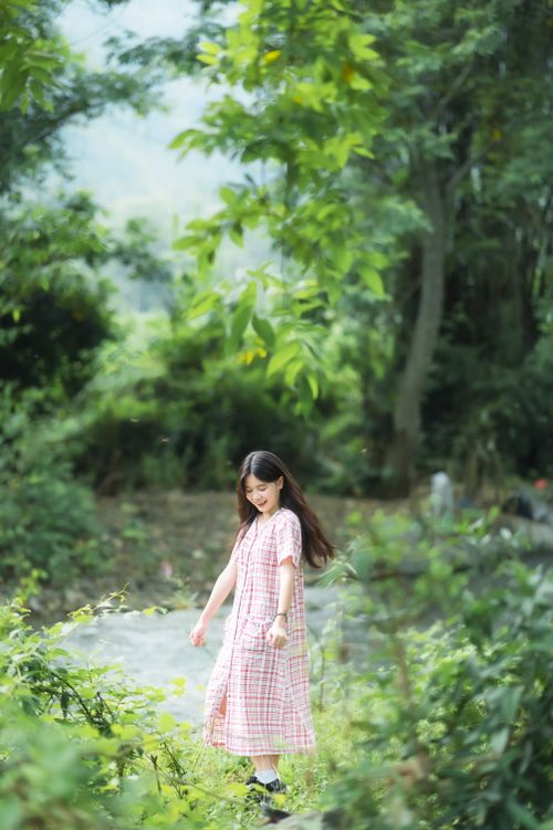 Free A young woman in a plaid dress standing amidst lush greenery in a serene outdoor setting. Stock Photo