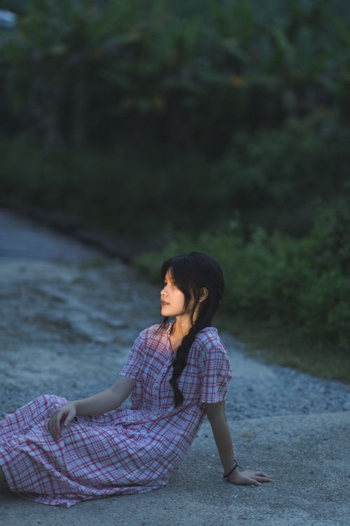 Free A young woman in a plaid dress sits outdoors in Lạng Sơn, evoking a peaceful evening mood. Stock Photo
