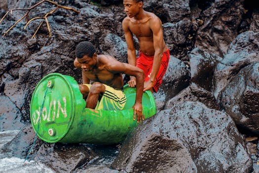 Two young men enjoying a summer adventure with a homemade barrel raft on rocky shores.
