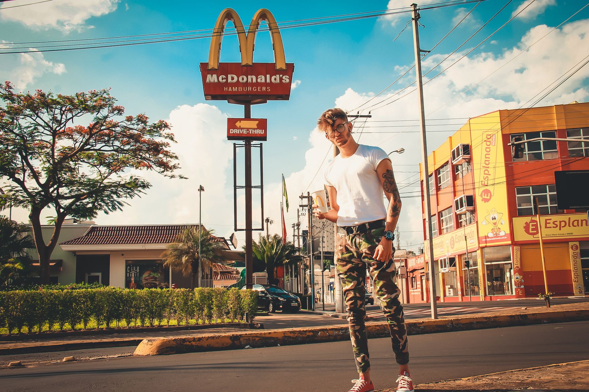 A fashionable man poses in an urban area near a McDonald's sign on a sunny day.