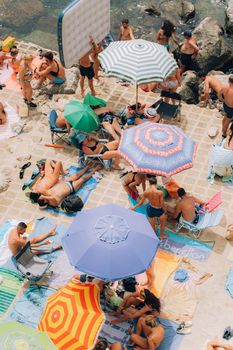 Colorful beach umbrellas and sunbathers at Santa Cesarea Terme, Italy, create a lively summer scene.