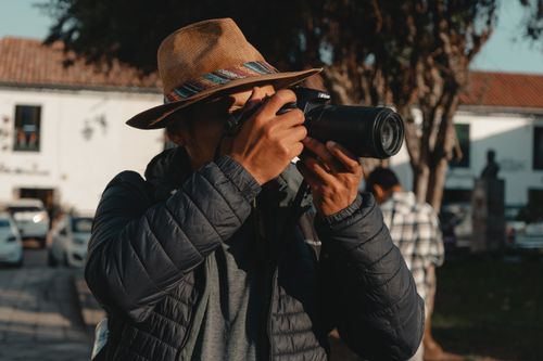 Free A man in a fedora hat photographing outdoors with a camera. Stock Photo