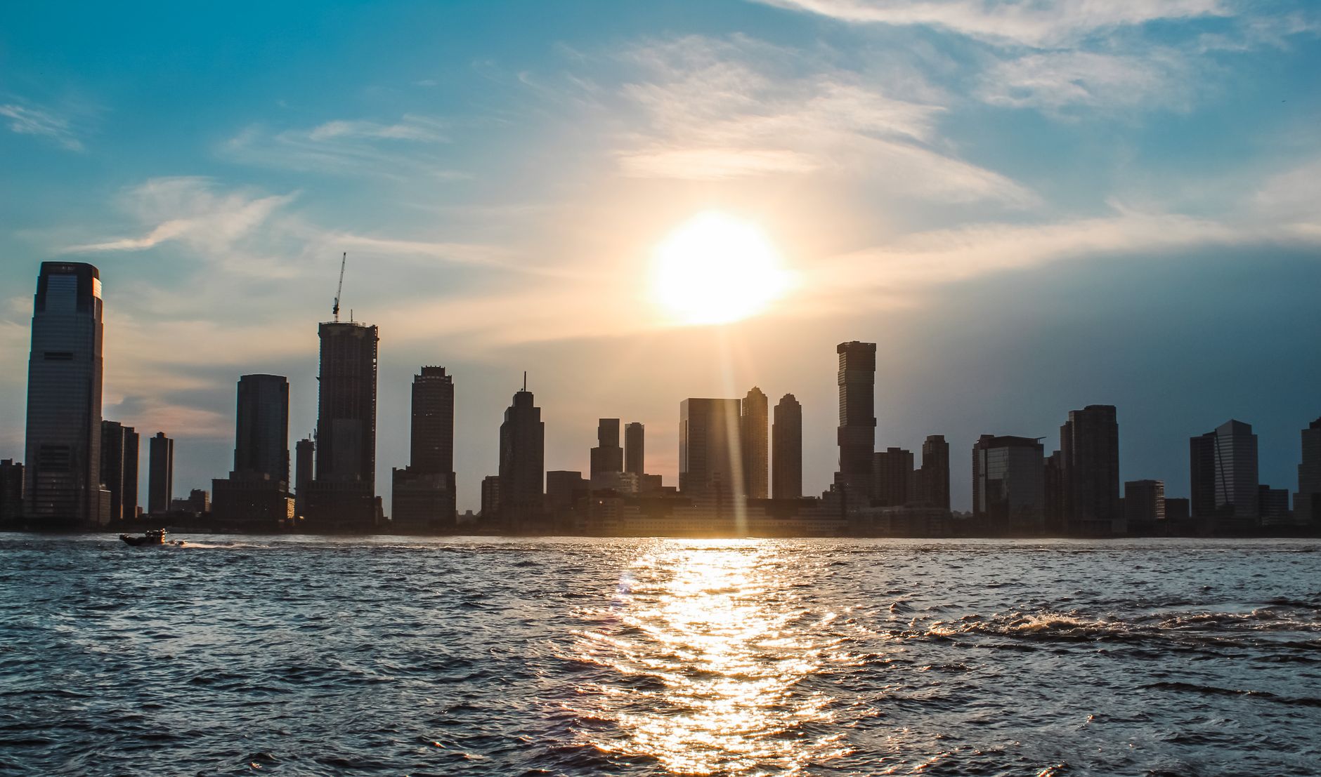 Silhouette of a city skyline at sunset with water reflecting the sunlight, highlighting urban structures.