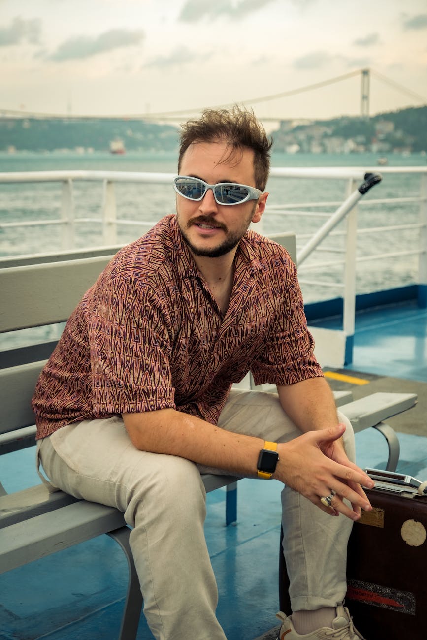 Un homme assis sur un ferry avec une valise, contemplant la mer.