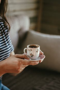Close-up of a woman holding a floral-patterned coffee cup indoors.