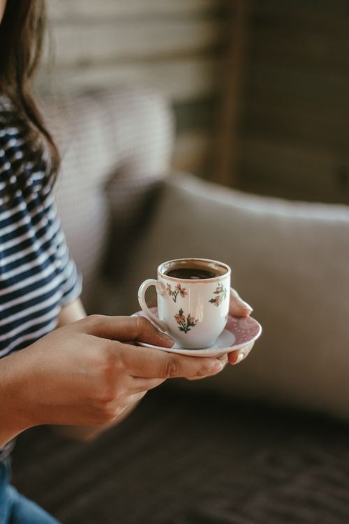 Free Close-up of a woman holding a floral-patterned coffee cup indoors. Stock Photo