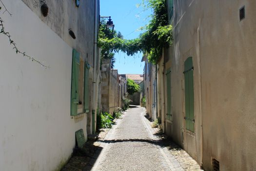 A picturesque narrow street in a historic European town with sunlit stone paths and quaint architecture.