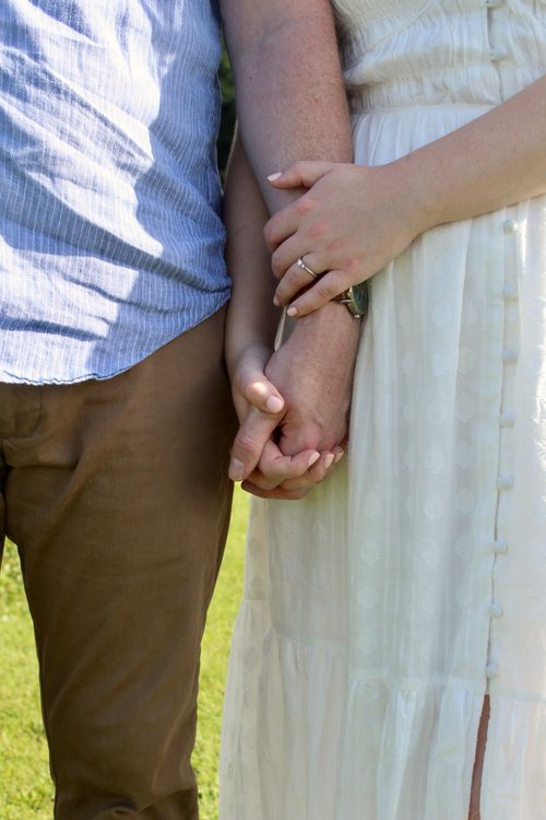 Free A close-up of a couple holding hands outdoors, showcasing an engagement ring in summer. Stock Photo