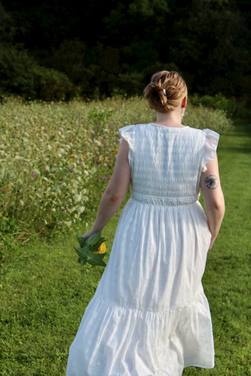 Back View of a Woman in a White Dress Walking on a Meadow 