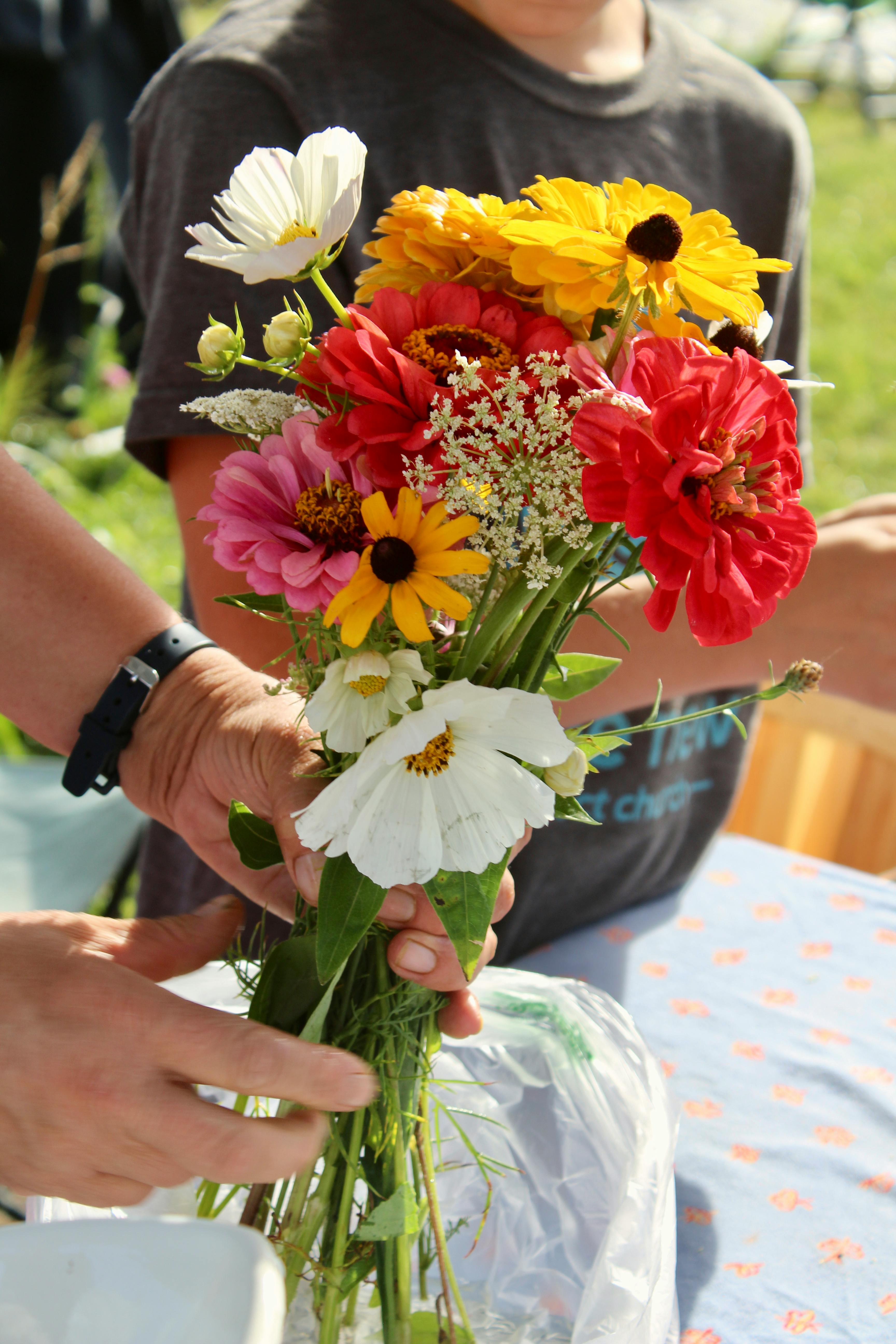 A colorful bouquet of fresh wildflowers held by a child outdoors in a sunny setting.