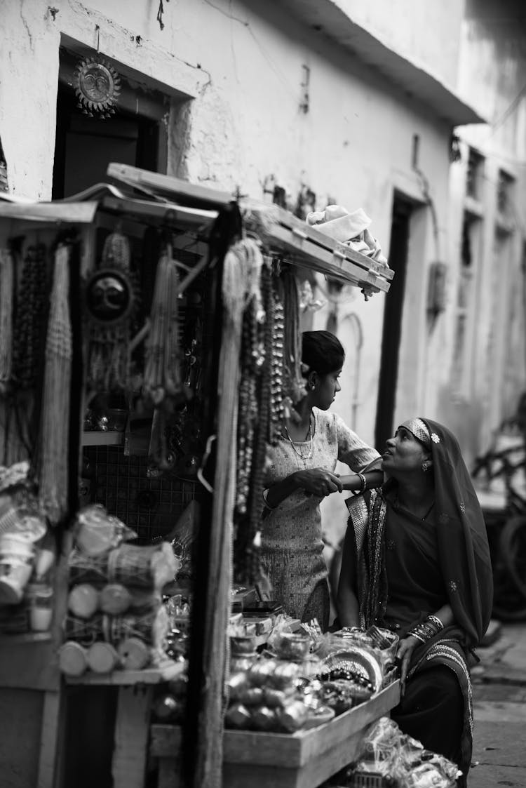 Candid Shot Of A Woman Sitting Next To A Market Stall In Front Of A Building 