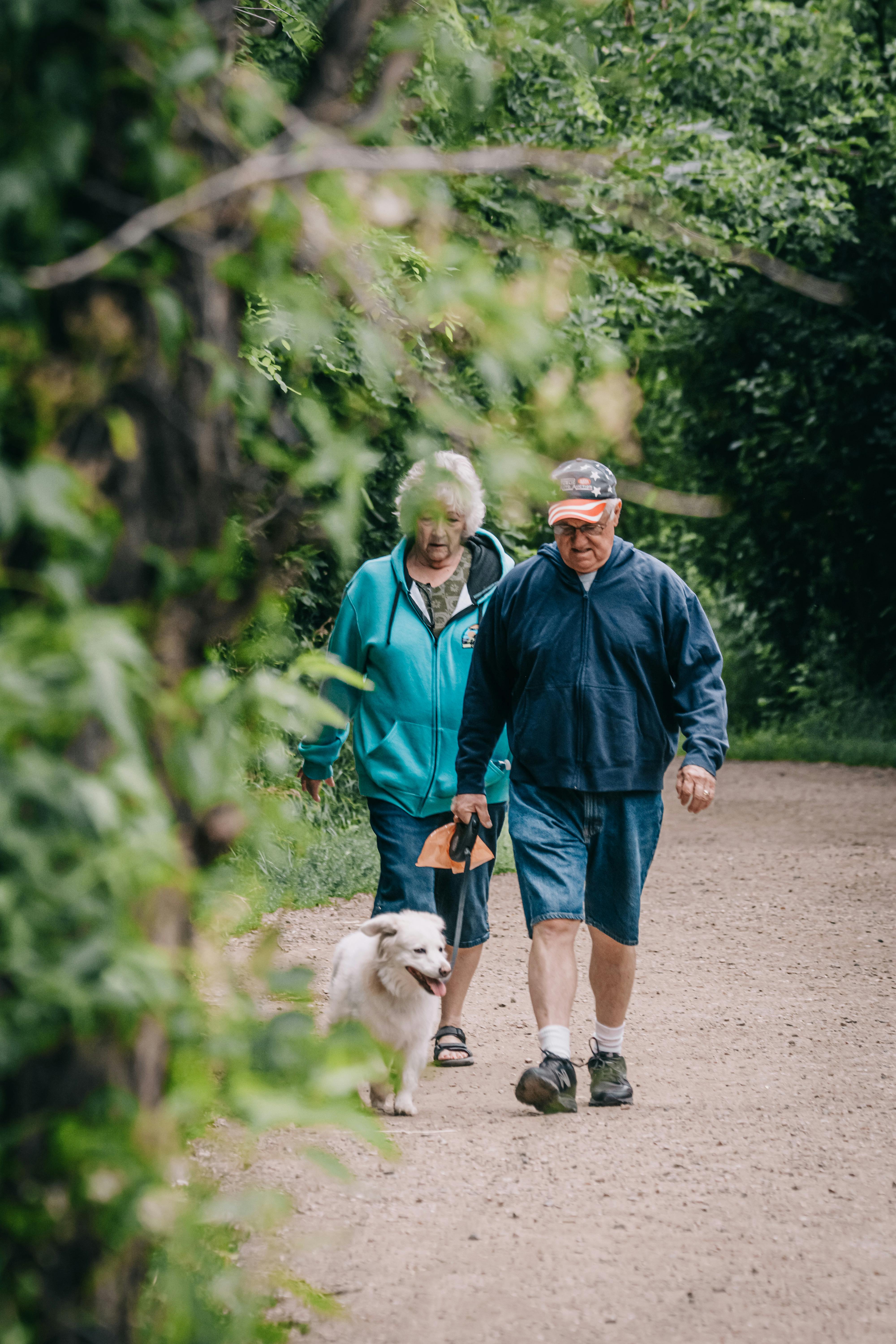An older couple walking through a park with their dog, suggesting the ordinary routines that remain relevant even as obesity treatment becomes more pharmaceutical.