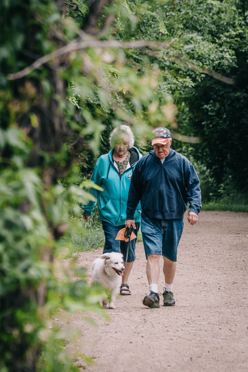 An older couple walking through a park with their dog, suggesting the ordinary routines that remain relevant even as obesity treatment becomes more pharmaceutical.