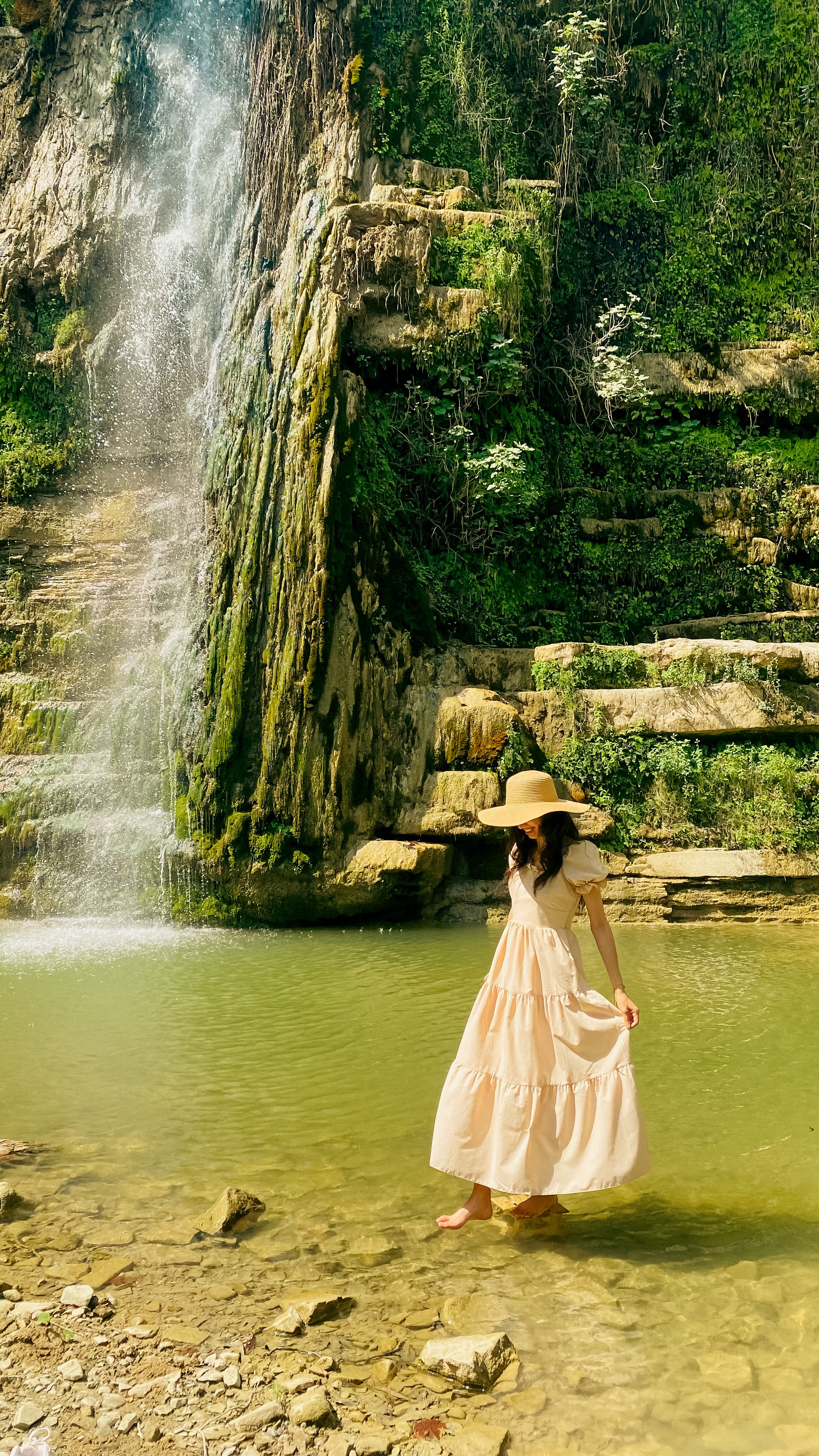 Serene scene of a woman in a sunhat and maxi dress standing by a waterfall.