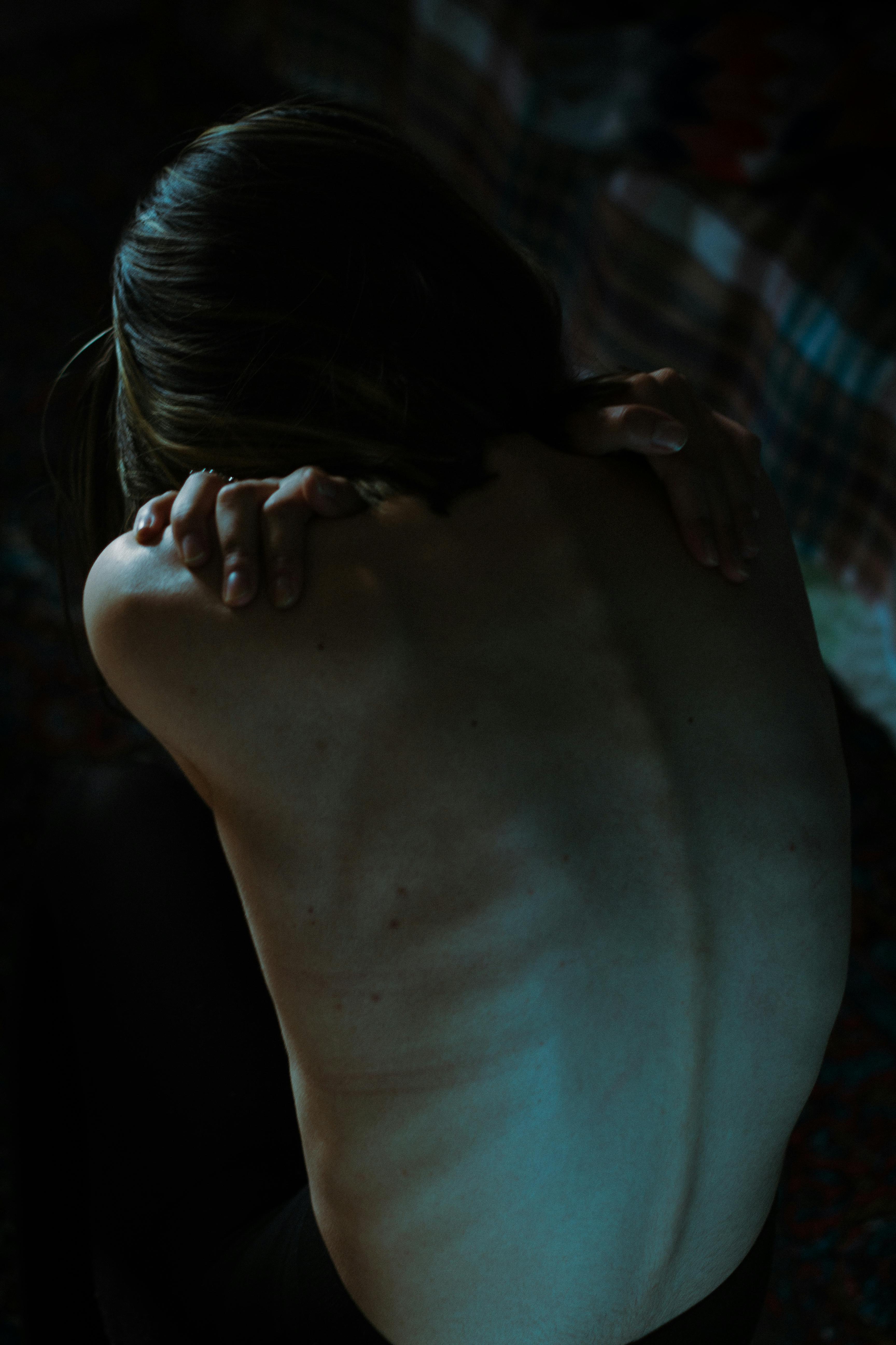 A dramatic nude portrait of a woman in dim light, showcasing an artistic and emotional composition.