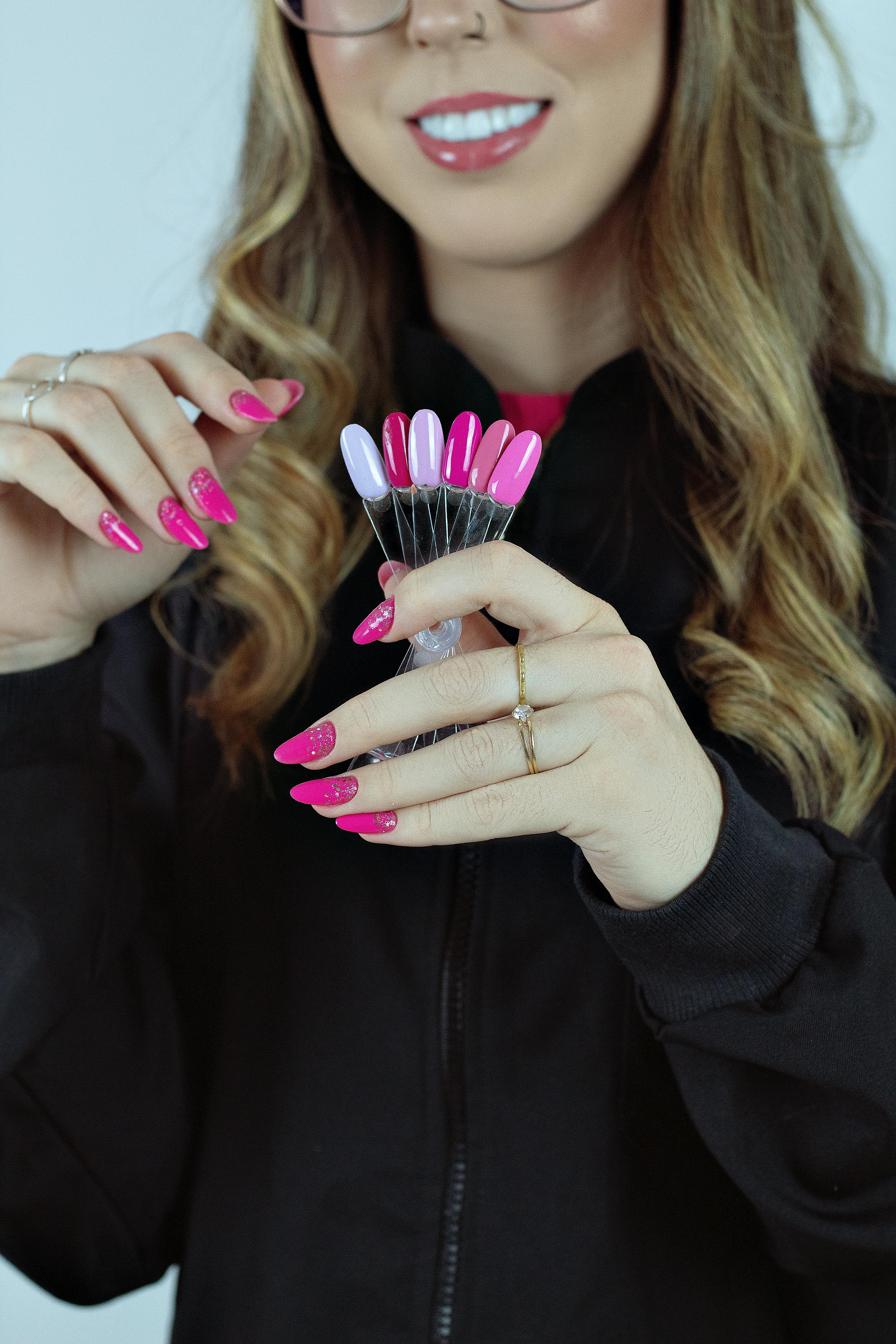 Smiling woman holding pink nail color samples in a studio setting.