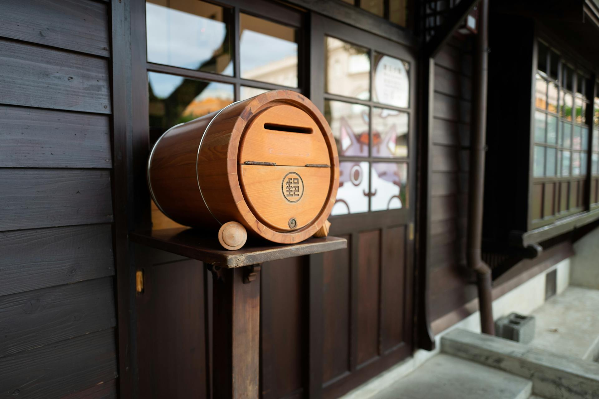 Wooden barrel mailbox mounted outside a building with wooden facade and glass windows.