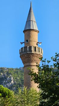 Scenic view of a traditional minaret in Amasya, Türkiye, against a backdrop of mountains and trees.