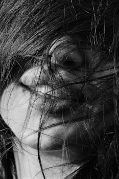 Close-up black and white portrait of a woman with tousled hair covering her face.