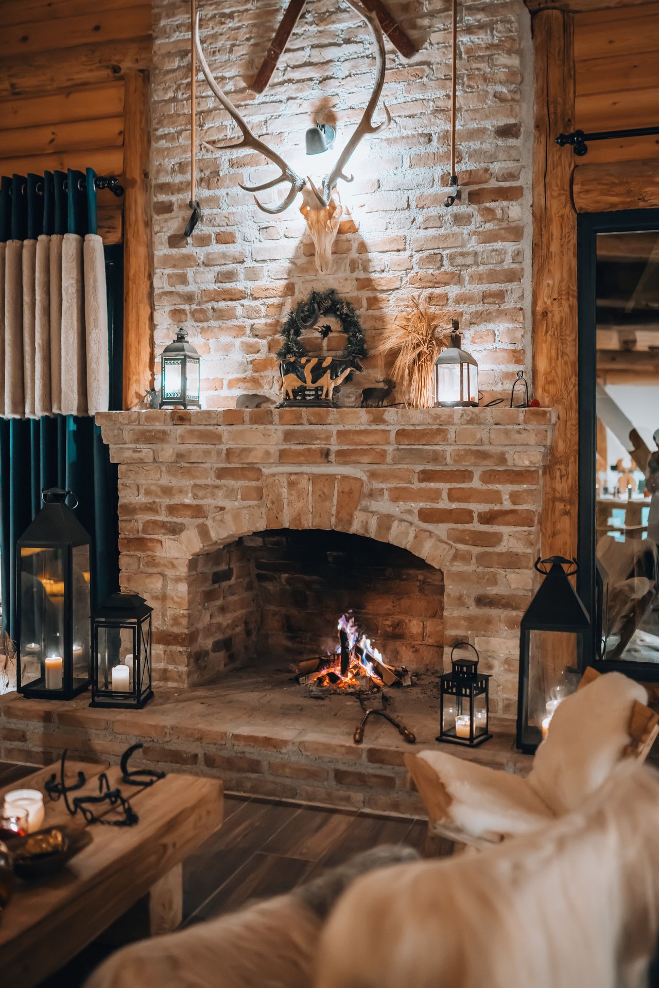 Rustic brick fireplace with burning fire, antlers, and lanterns on the mantel