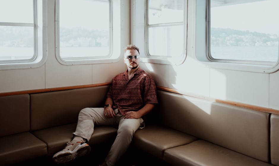 A fashionable man in sunglasses sits on a ferry in Istanbul under the afternoon sun.