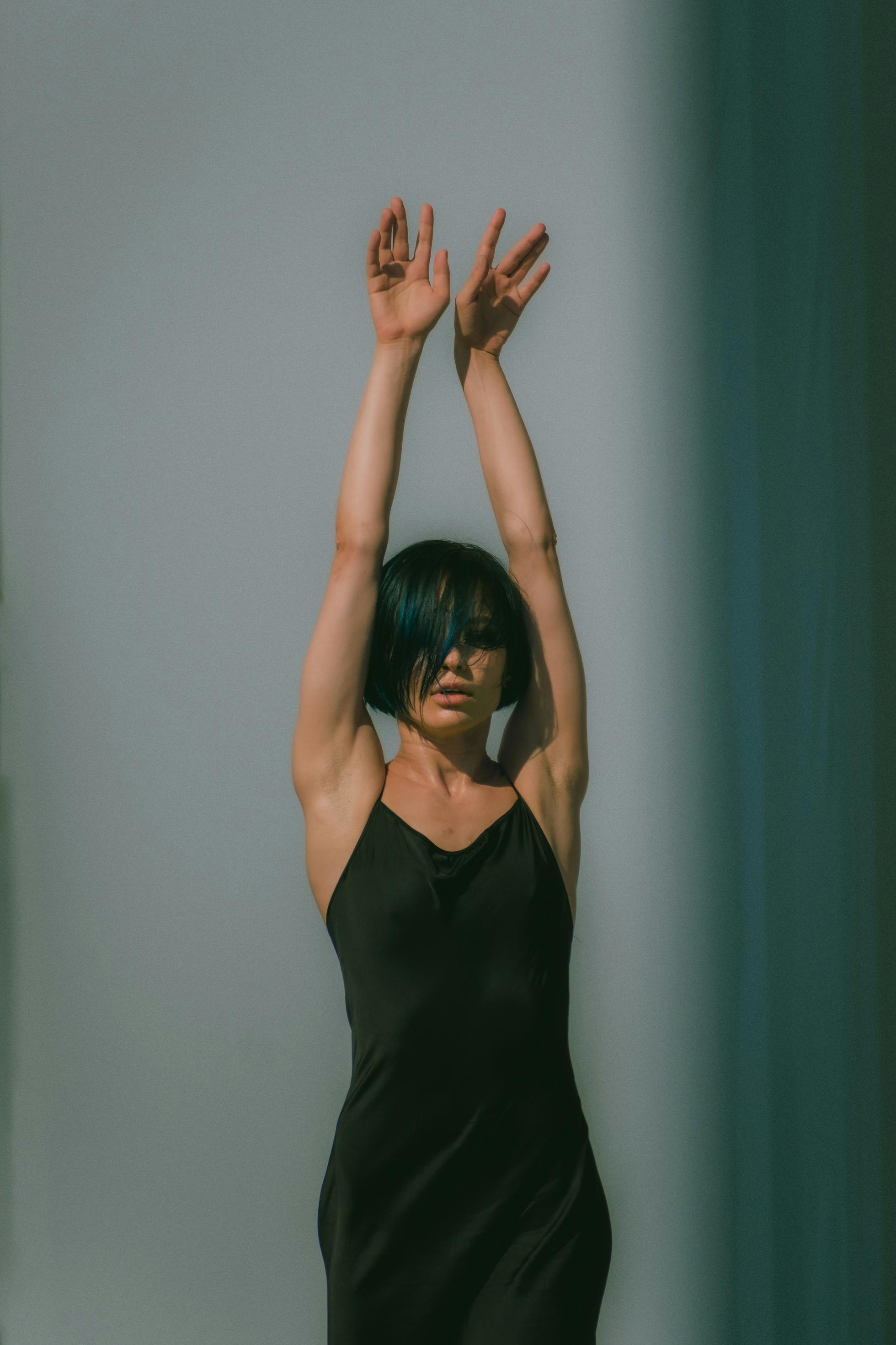 Free Artistic portrait of woman in black dress with arms raised against white background. Stock Photo