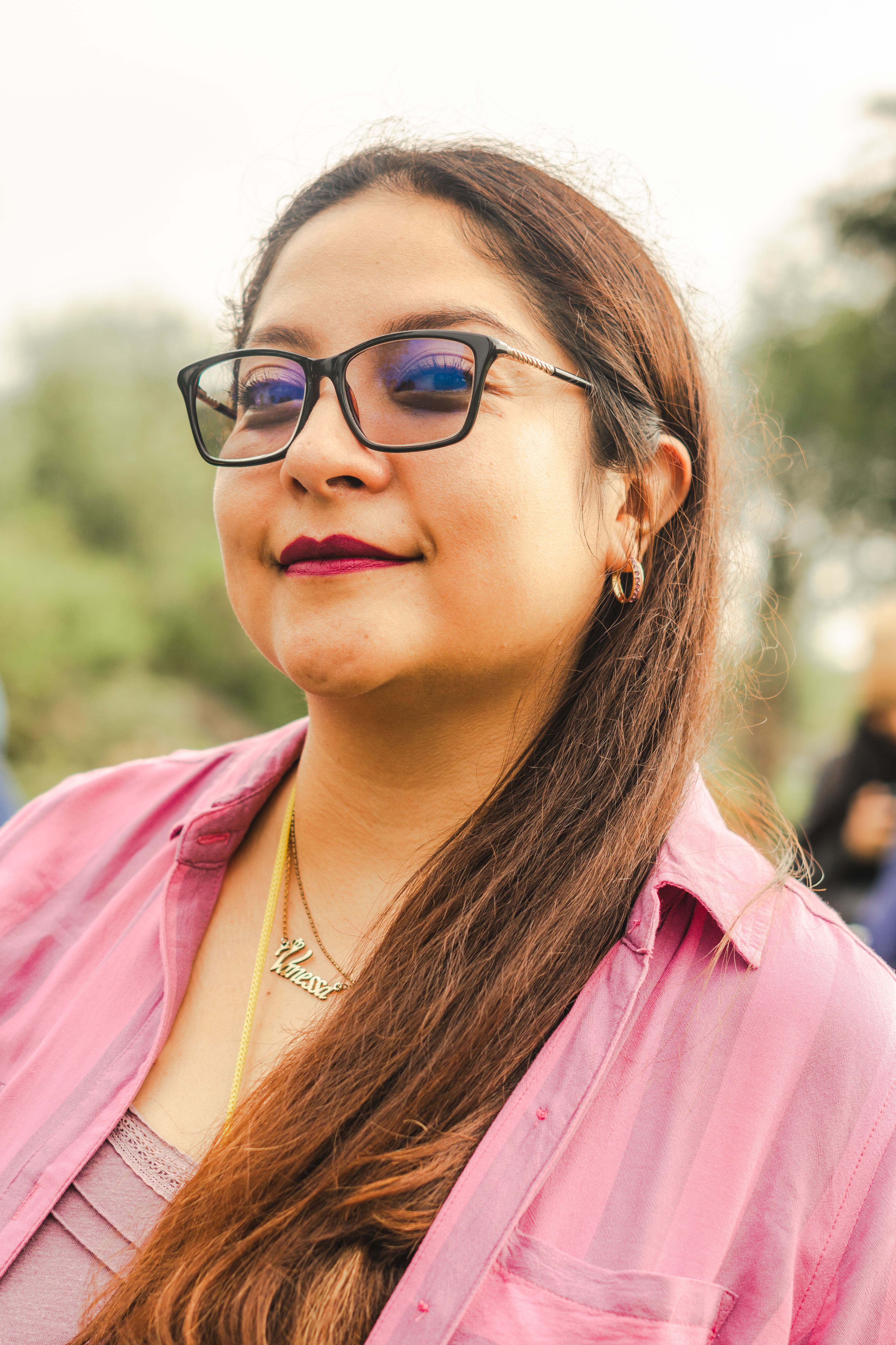 A woman with eyeglasses and long hair smiles confidently outdoors in Mexico City.