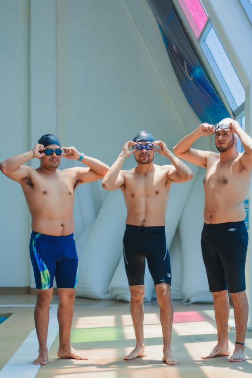Free Three shirtless men with swim caps and goggles prepare by the indoor pool. Ready for a swim match. Stock Photo