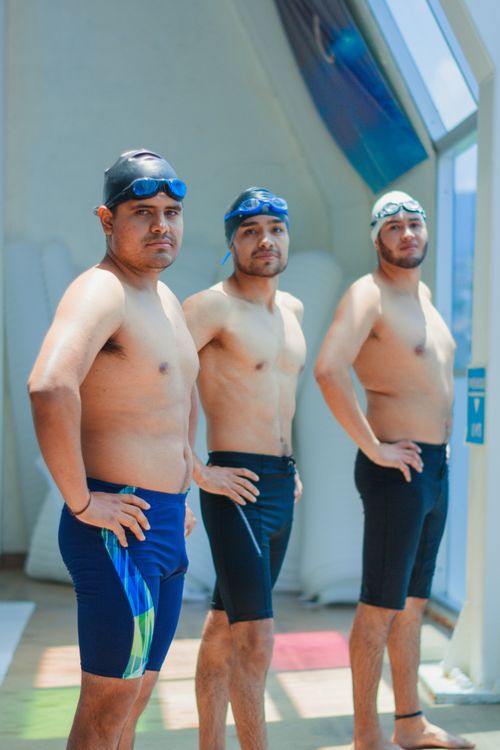 Free Three male swimmers pose with confidence indoors, wearing swim caps and goggles. Stock Photo