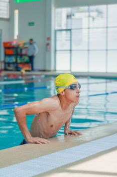 A young male swimmer with a yellow swim cap and goggles emerging from the pool.