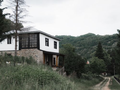 Free A charming house in a rural setting with lush green hills, trees, and a dirt road, perfect for peaceful retreats. Stock Photo