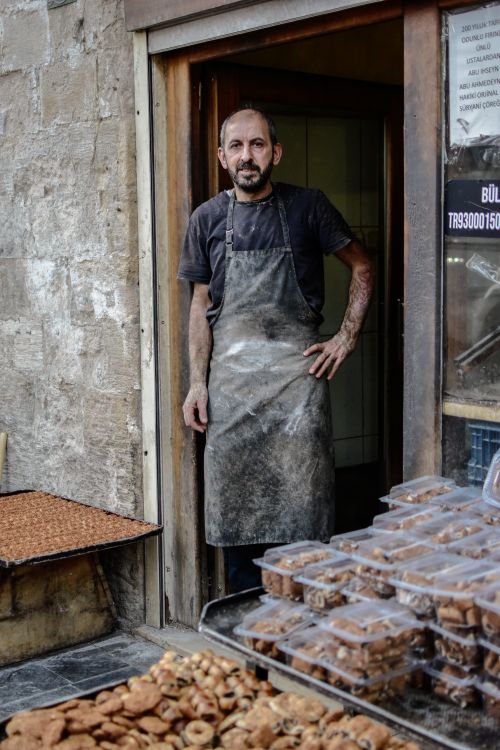 Free Baker in apron stands at shop door, showcasing a variety of fresh cookies. Stock Photo