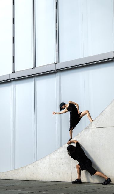Two dancers striking a pose against a modern urban building exterior, showcasing movement and architecture.
