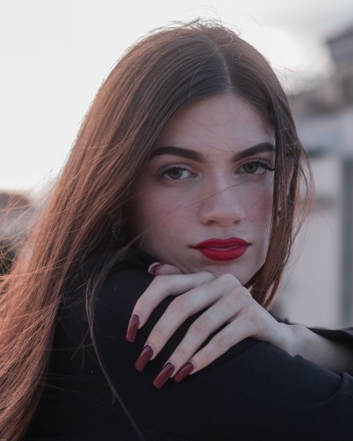 Free A captivating portrait of a woman with red lipstick, long hair, and confident expression in an outdoor setting. Stock Photo