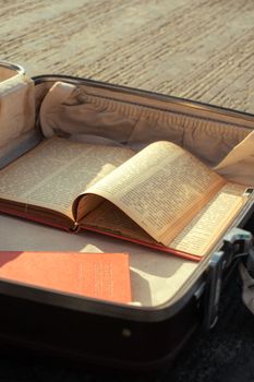 A vintage open book inside a sunlit suitcase, evoking a sense of nostalgia and travel.