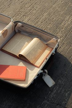 An open vintage suitcase filled with books on a textured pavement, evoking travel nostalgia.