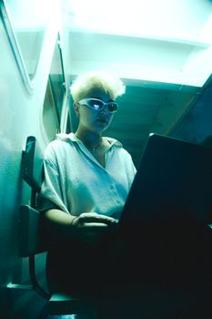 Blonde adult using laptop with cool lighting. Creative indoor setting.