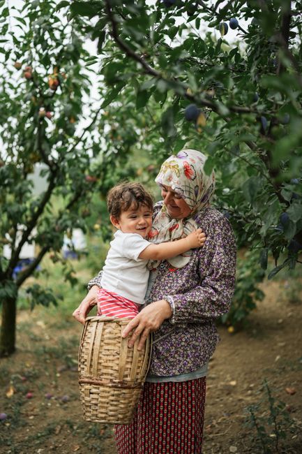 A grandmother and child sharing a joyful moment in a lush orchard, surrounded by greenery.