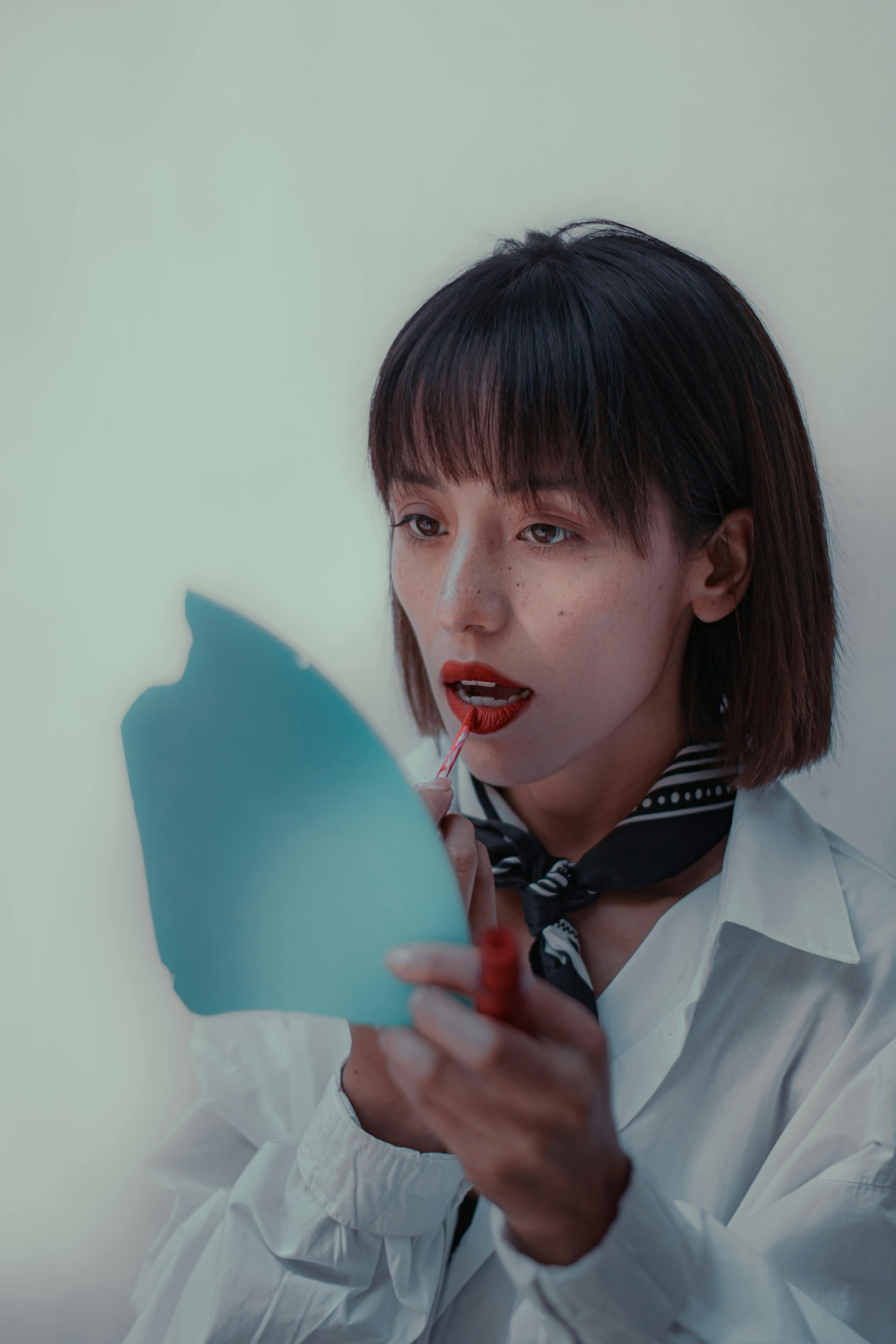Elegant woman applying red lipstick in a refined indoor setting.