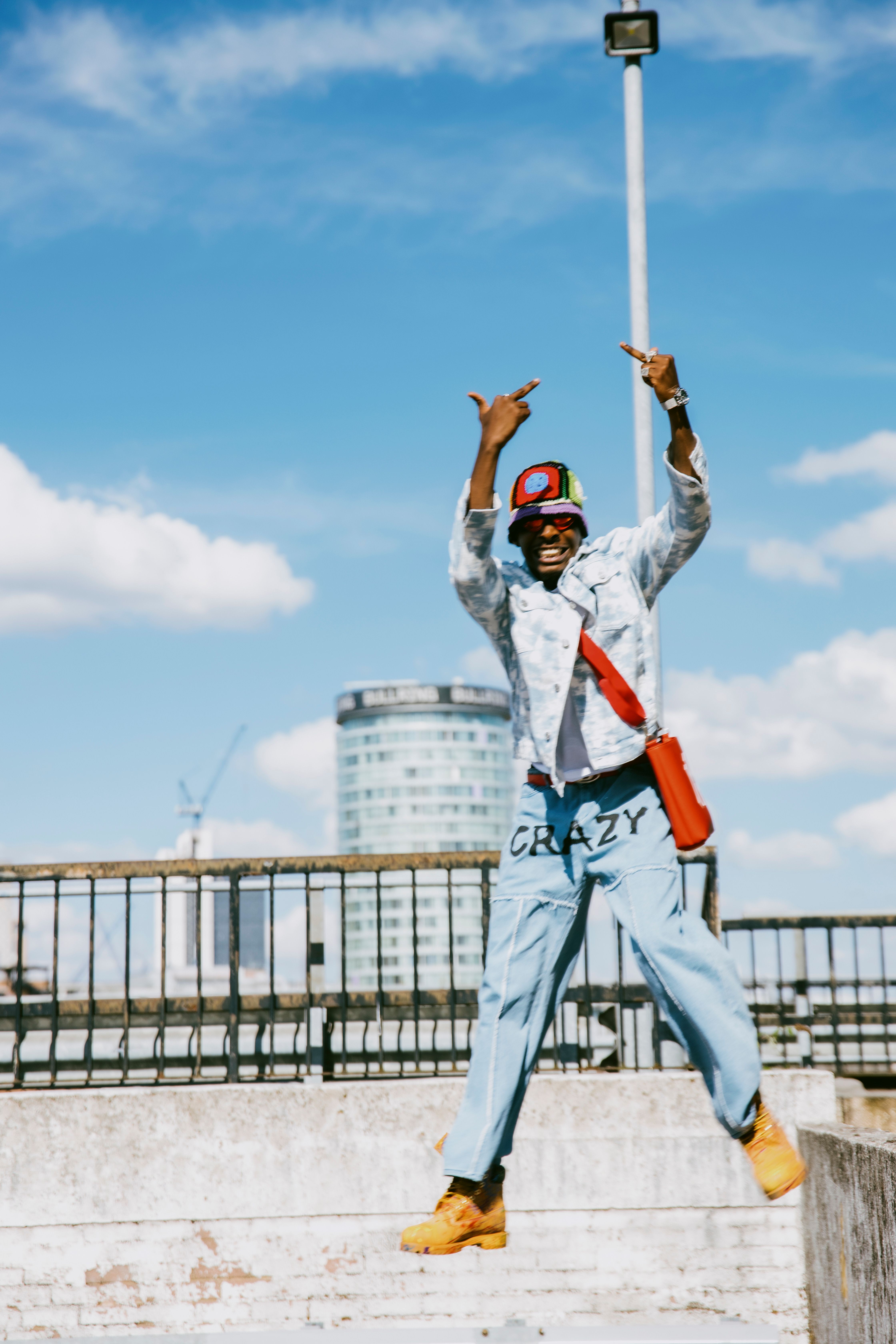 Stylish man in urban setting making a confident gesture against a blue sky.