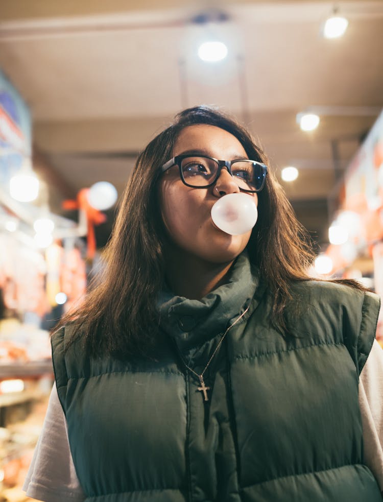 Young Woman In Puffer Vest Blowing A Chewing Gum Bubble