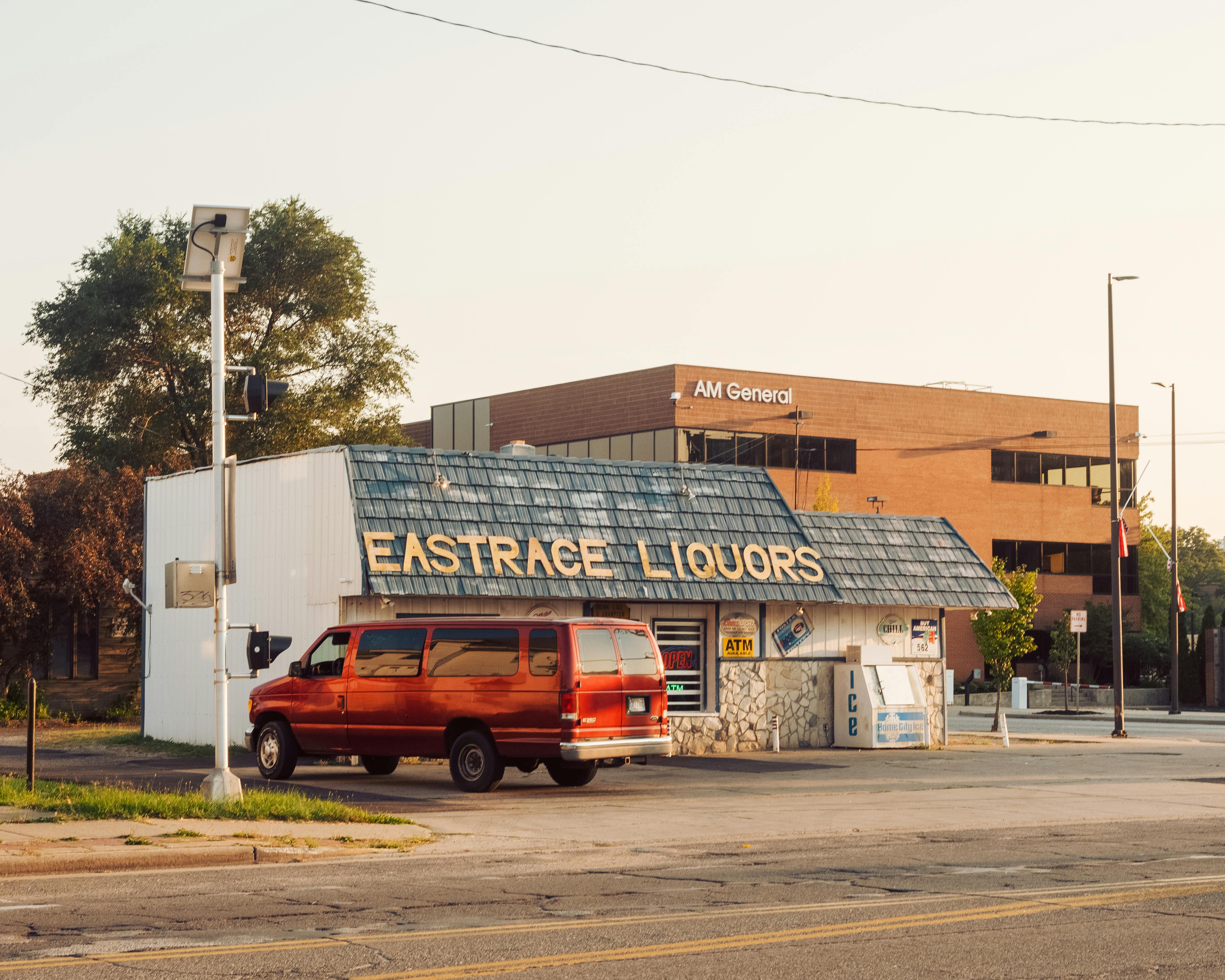 A vibrant street scene featuring a liquor store and parked vintage red van under a clear sky.