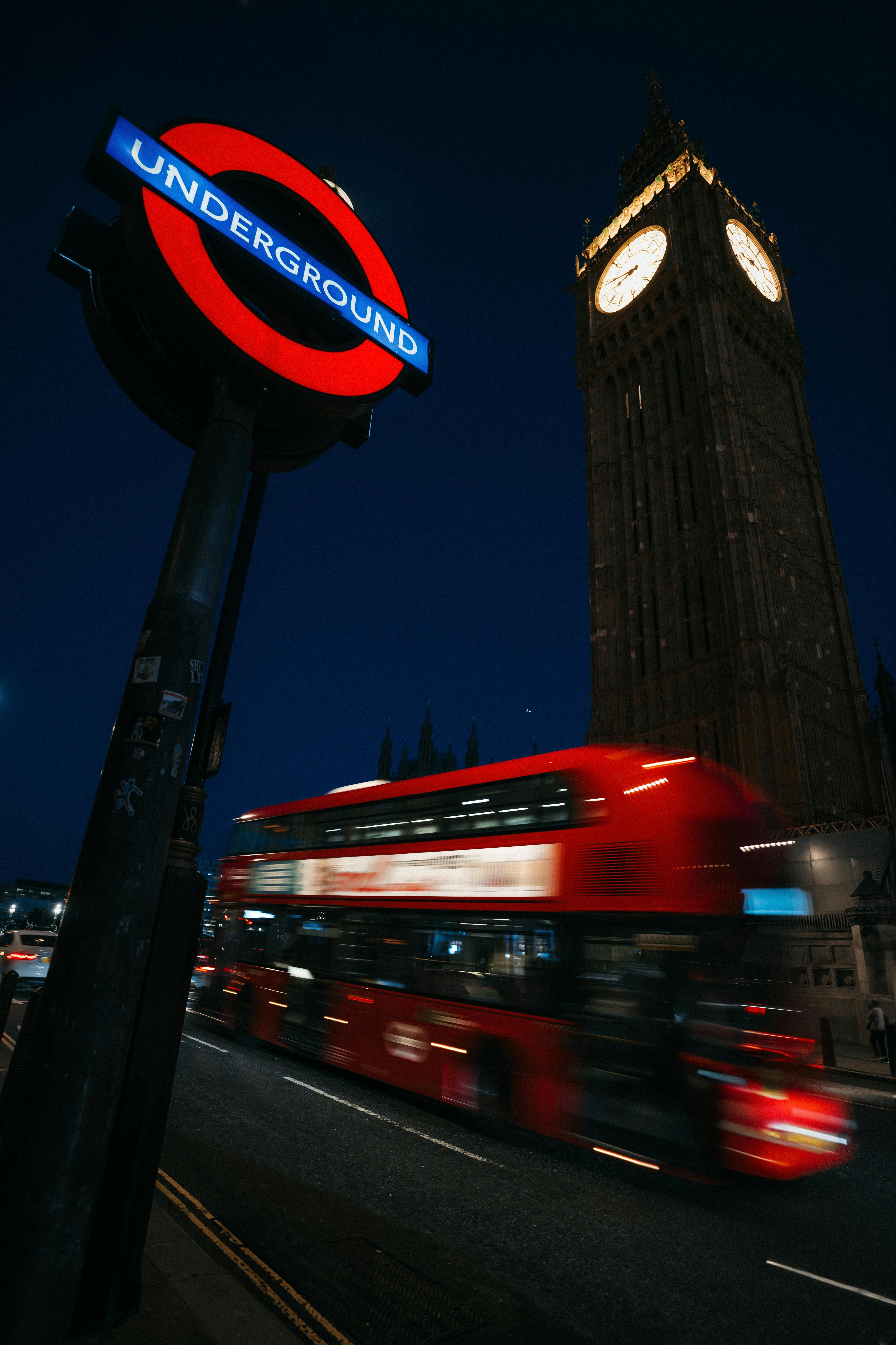 Vibrant night view of London with Big Ben and a moving double-decker bus by the underground sign.
