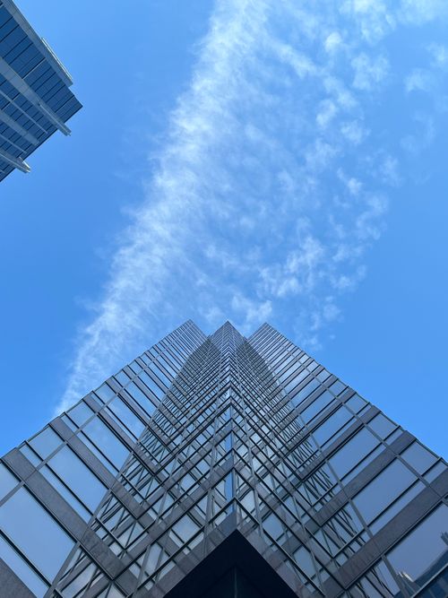 Free Low angle view of a sleek glass skyscraper against a vibrant blue sky with wispy clouds. Stock Photo