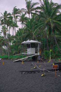 Photo by Nitro Lifeguard tower at Hana's tropical black sand beach, framed by lush palm trees.