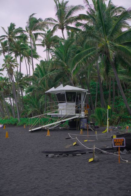 Photo by Nitro Lifeguard tower at Hana's tropical black sand beach, framed by lush palm trees.