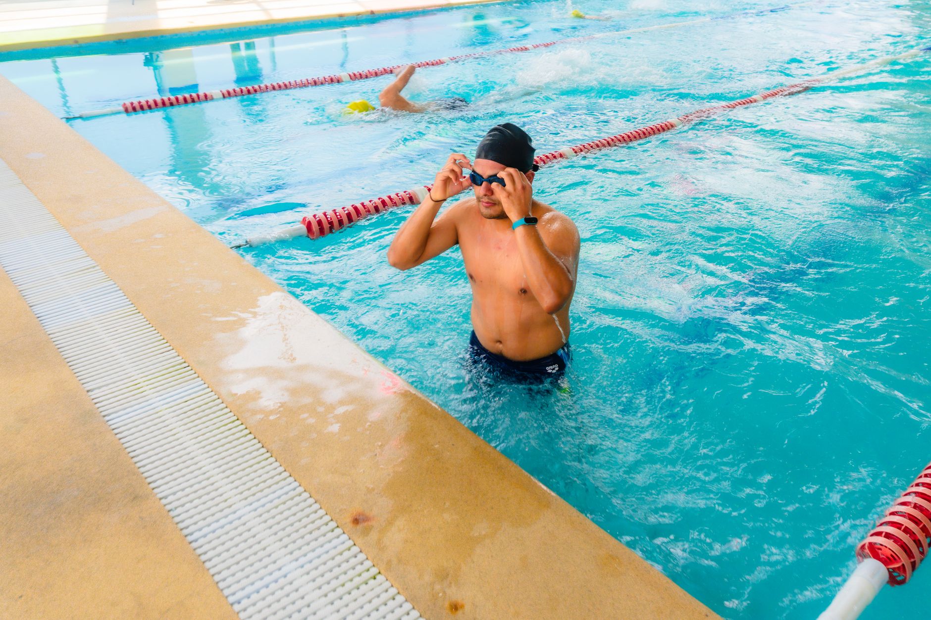 A male swimmer adjusts his goggles during training in an outdoor swimming pool.