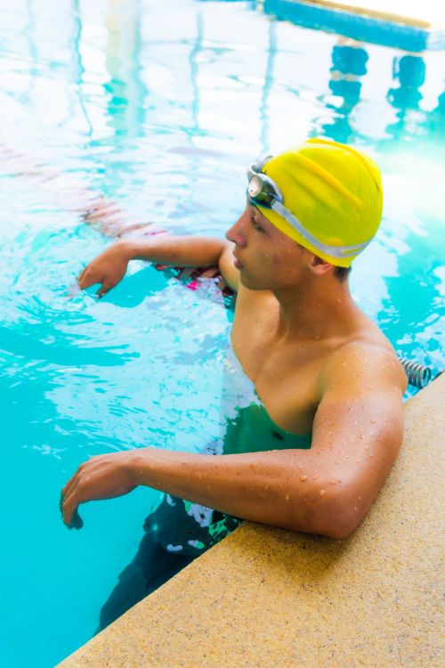 Free Swimmer in a yellow cap takes a break at a sunny poolside, showcasing fitness and leisure. Stock Photo