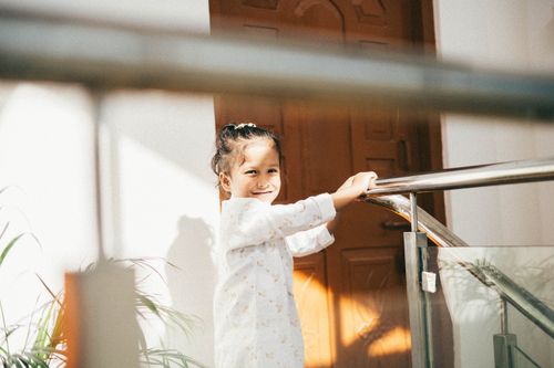 Free Cheerful girl in white shirt holding railing, bathed in natural light indoors. Stock Photo