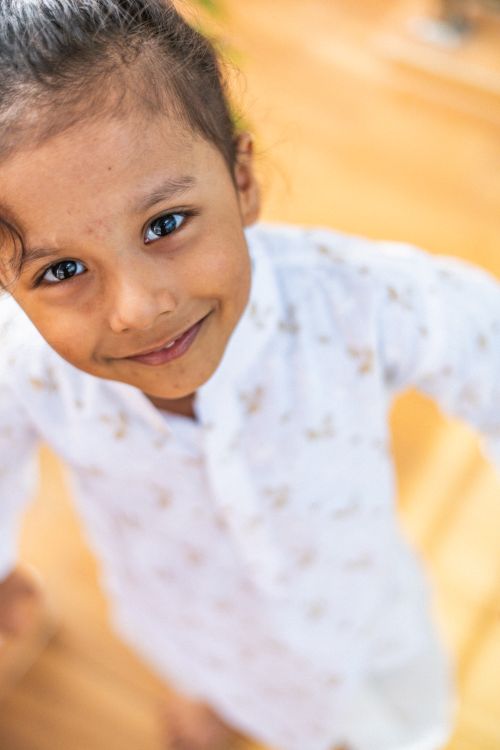 Free A cheerful young girl stands smiling in a white dress, exuding warmth and happiness. Stock Photo